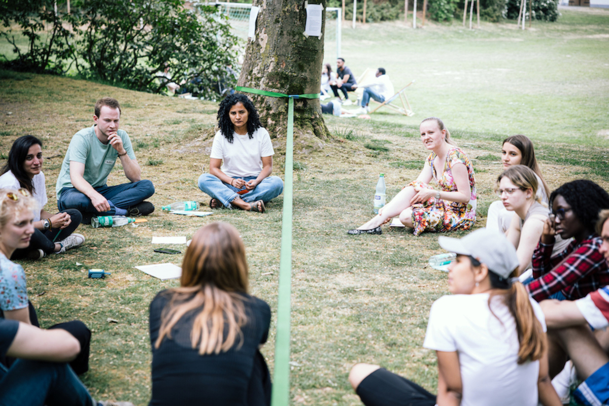 Junge Menschen sitzen bei einem Seminar auf einer Wiese