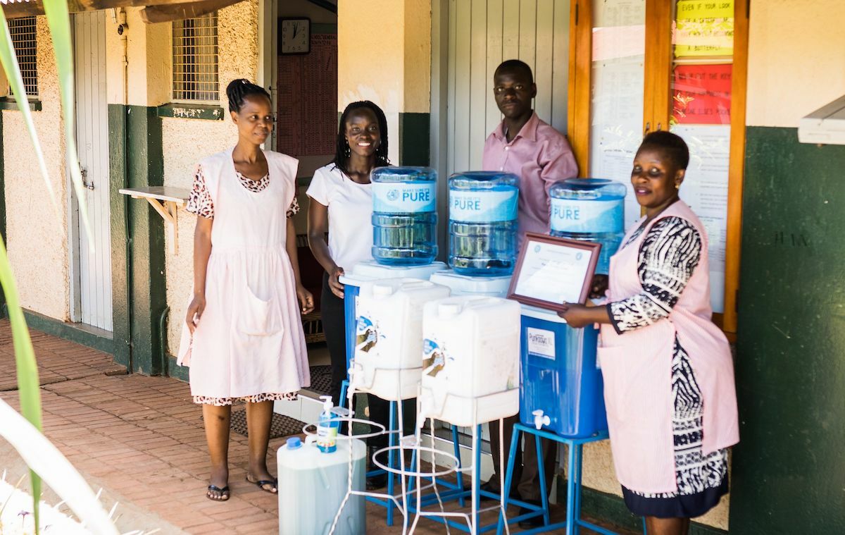 Junge Menschen aus Uganda informieren vor Wasserbehältern über Trinkwasseraufbereitung